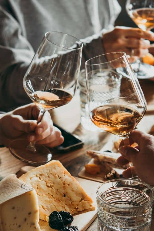 Raised wine glasses toasting over table laid with cheese plate