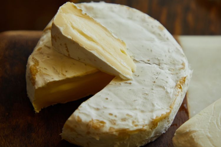A round of Camembert cheese with a wedge cut out of it. Wedge is on top of the round