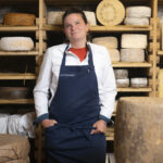 Nathalie Quatrehomme, standing in front of rounds of several cheeses