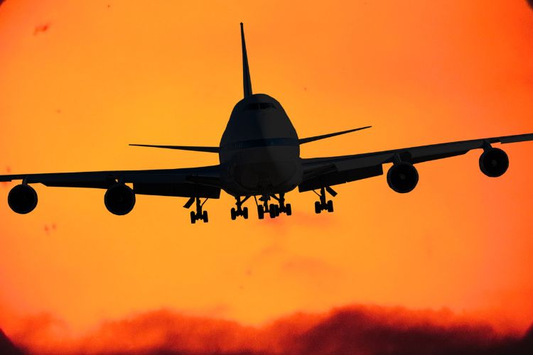 Silhouette of an airplane, behind it an orange sky